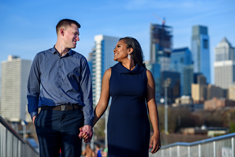 An engaged couple hold hands with the Philadelphia skyline behind them.